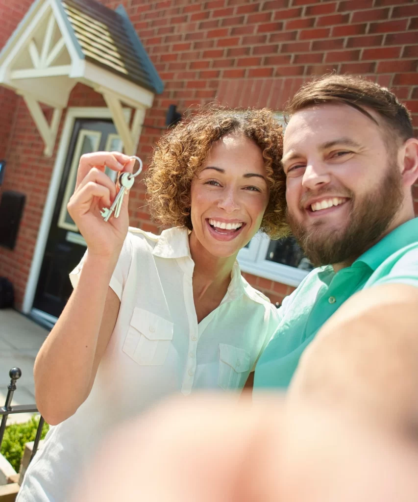 Happy couple standing in front of their new home, proudly holding keys, with CTM Insurance offering trusted home insurance coverage for peace of mind and protection.